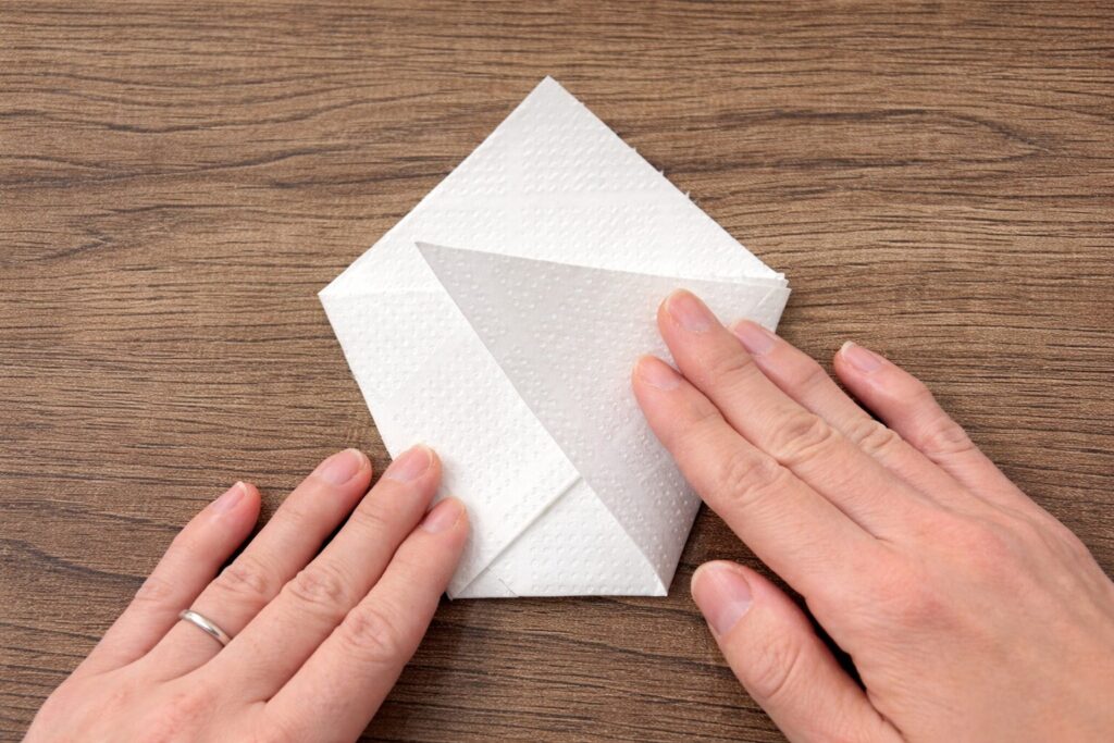 삼각형의 열린 부분이 위로 오도록 놓고, 좌우 모서리를 가운데로 접어 넣는다.